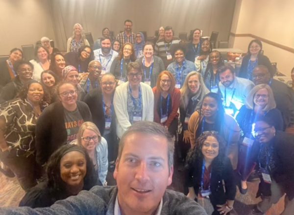 A large group of adults pose for a selfie.